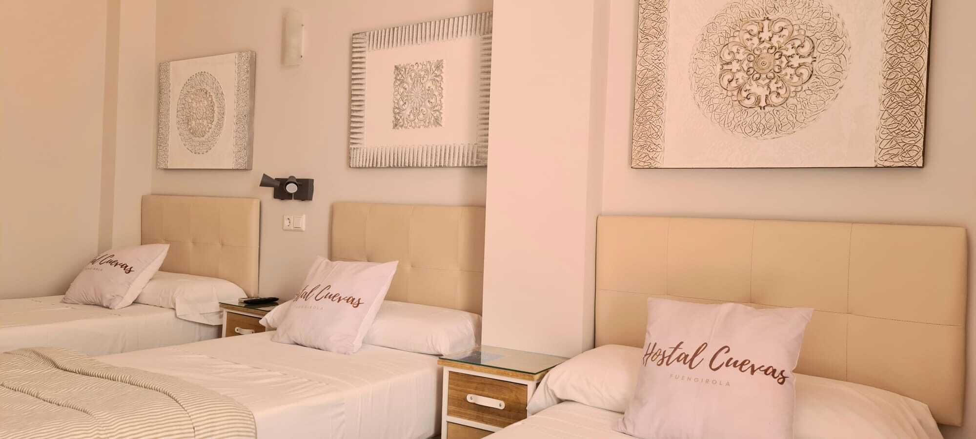 Habitación de hotel con tres camas, cada una con cabecera y almohada que dice "Hostal Cueras".