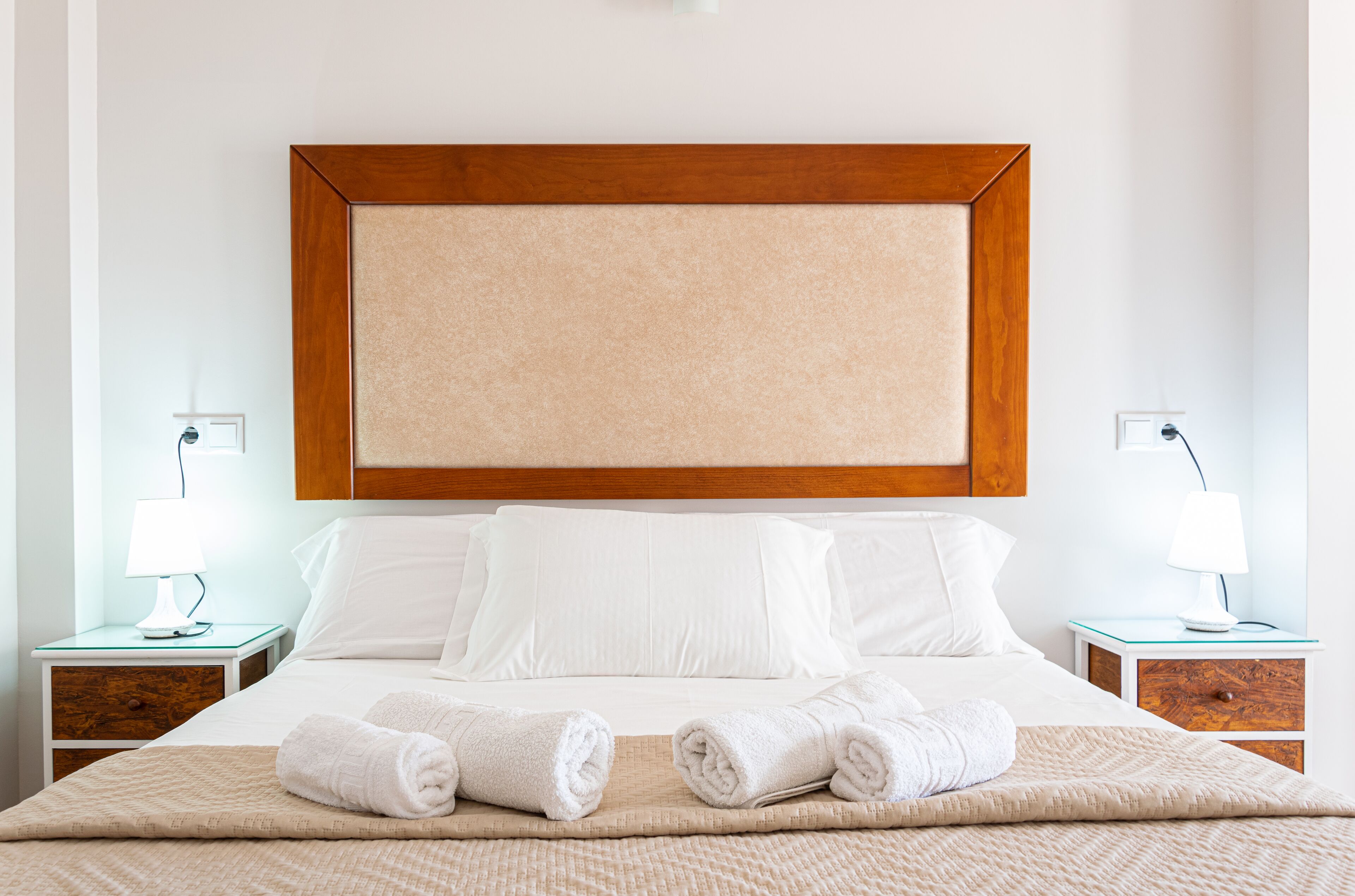 Una habitación de hotel con una cama grande, dos mesitas de noche, un cabecero de madera y ropa de cama blanca.