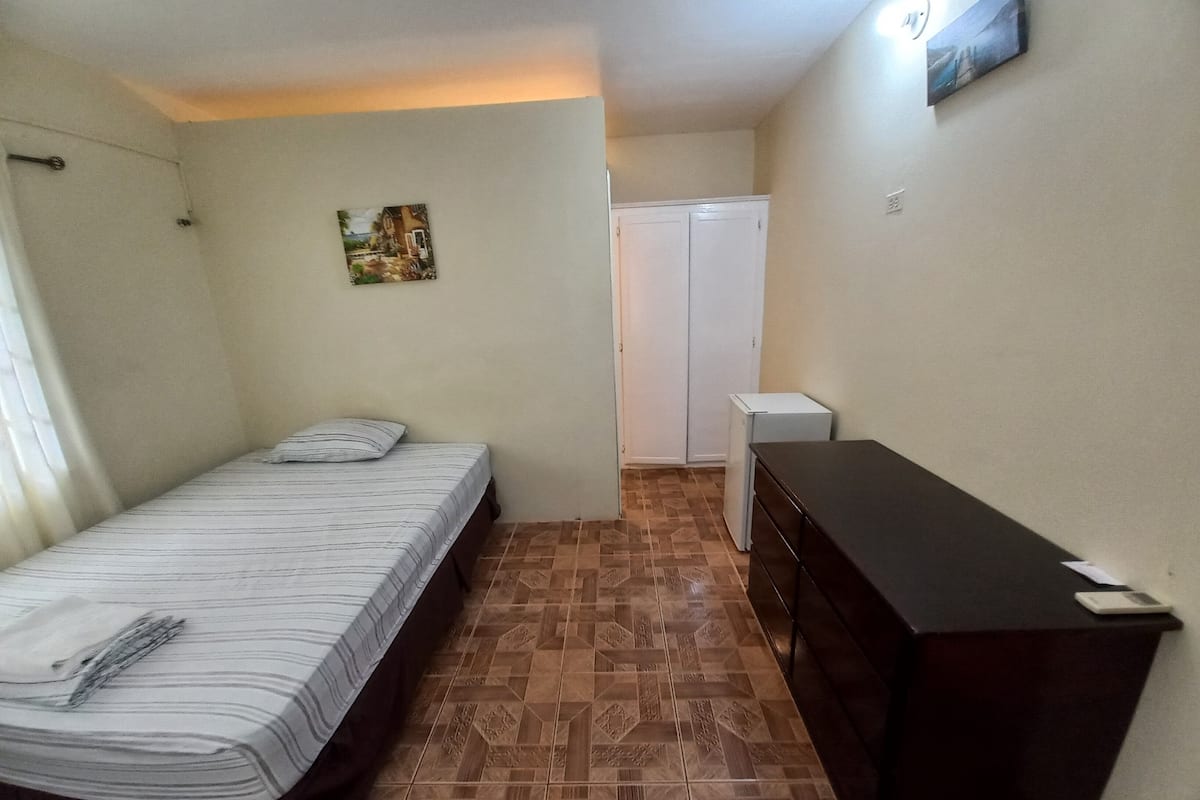 Una habitación pequeña y limpia con una cama, un aparador y un armario.