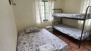 Una habitación con una cama individual, una litera, una mesita pequeña y una ventana con cortinas.