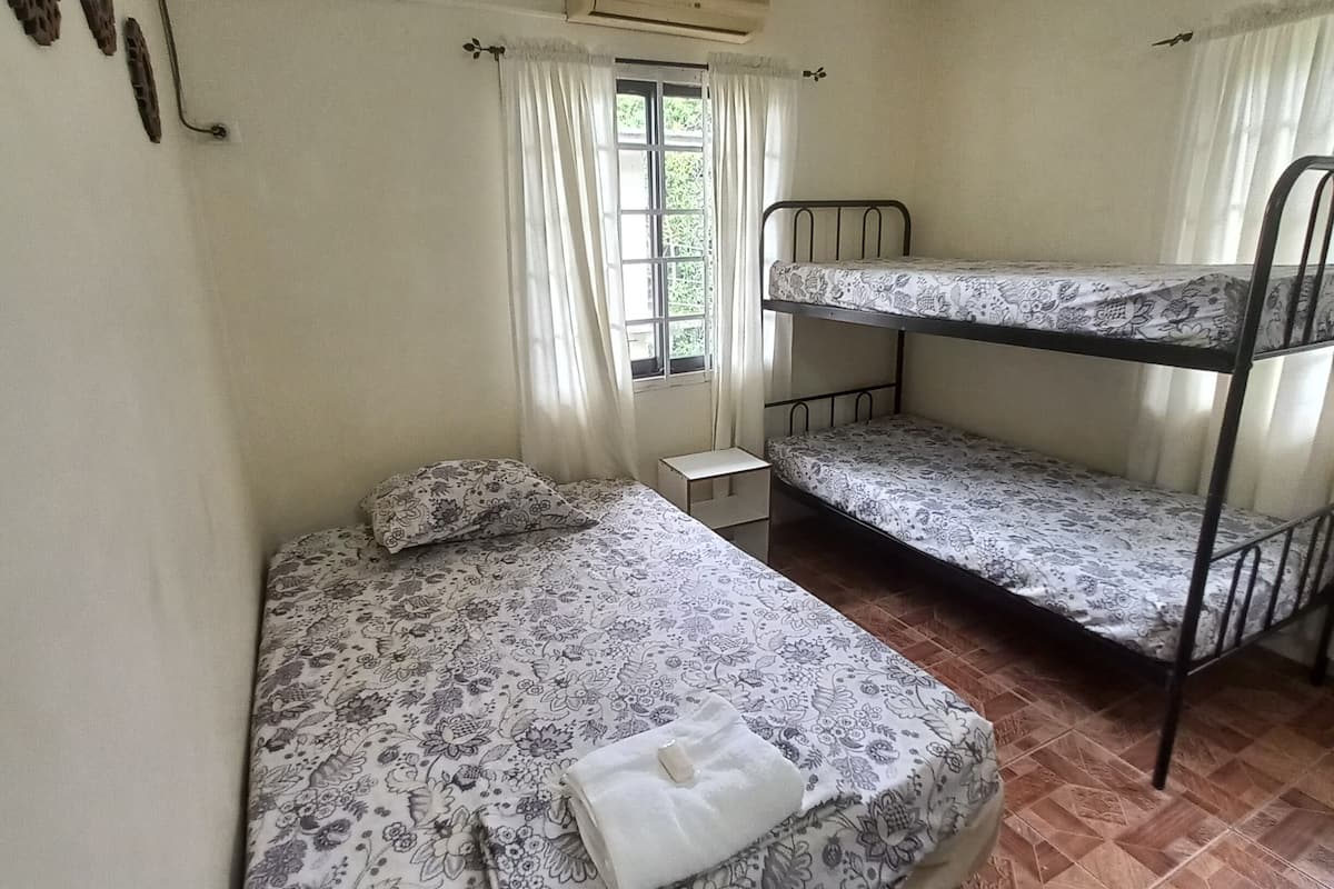 Una habitación con una cama individual, una litera, una mesita pequeña y una ventana con cortinas.
