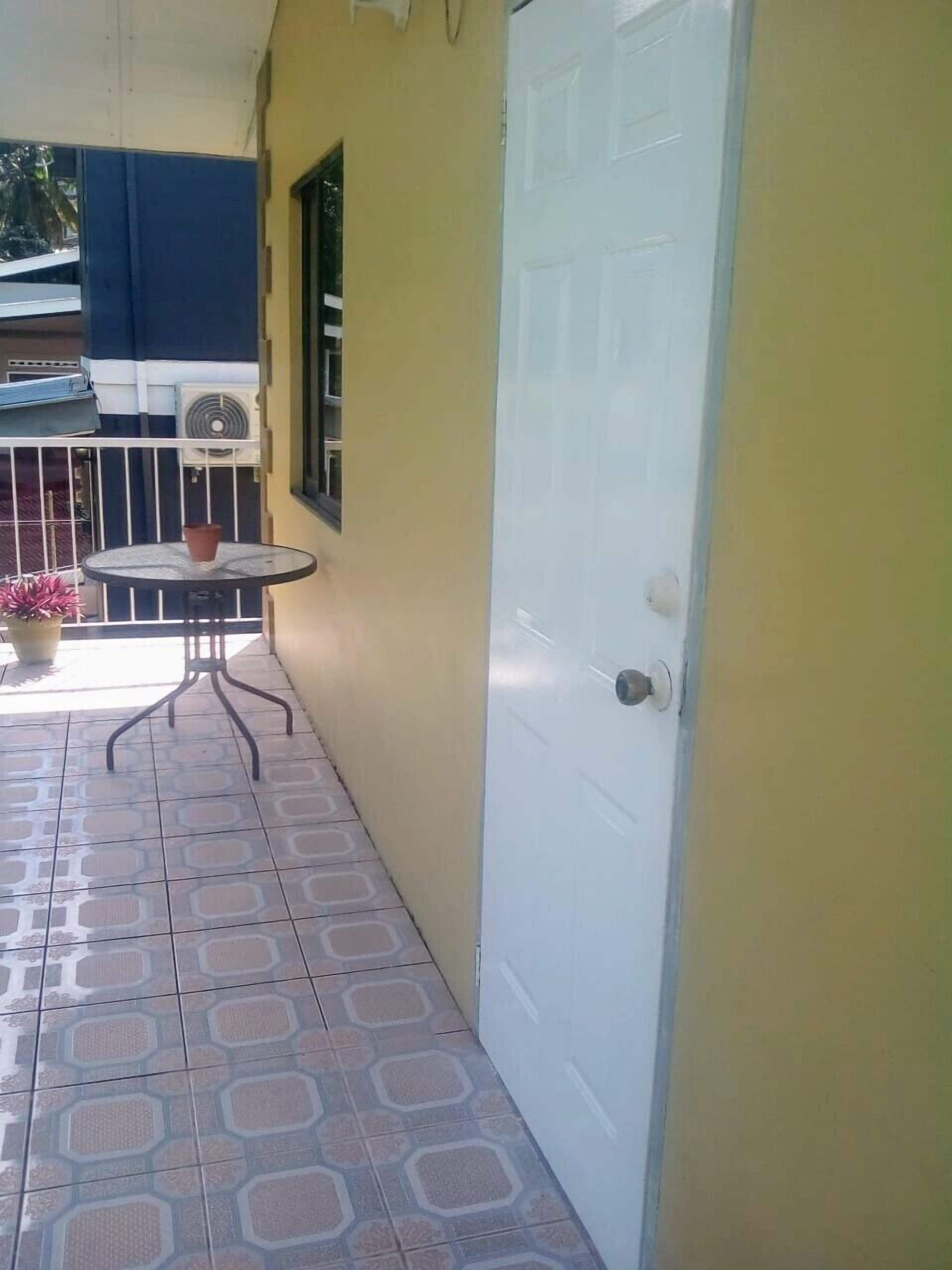 A small outdoor area with a tiled floor, a round table with a chair, a potted plant, and a white door.