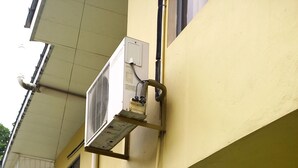 Un edificio amarillo con una puerta blanca, una escalera y unidades de aire acondicionado.
