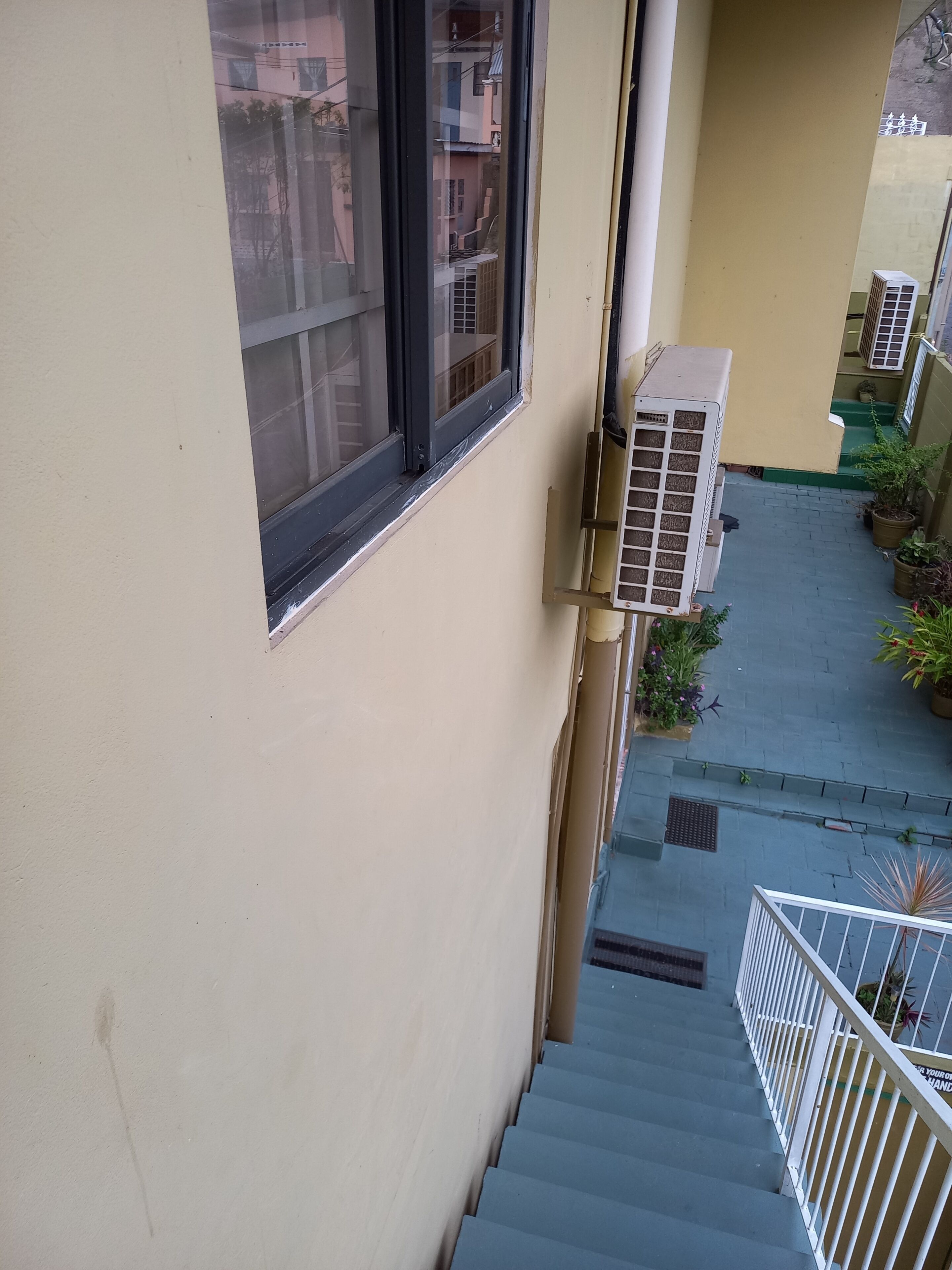 A residential building with a narrow staircase, outdoor air conditioning units, and potted plants.