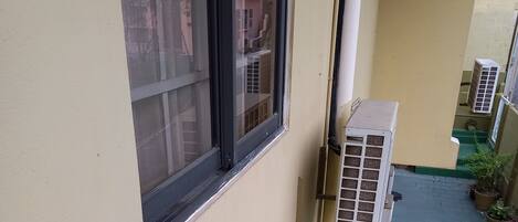 Un edificio residencial con una escalera estrecha, unidades de aire acondicionado exteriores y plantas en macetas.