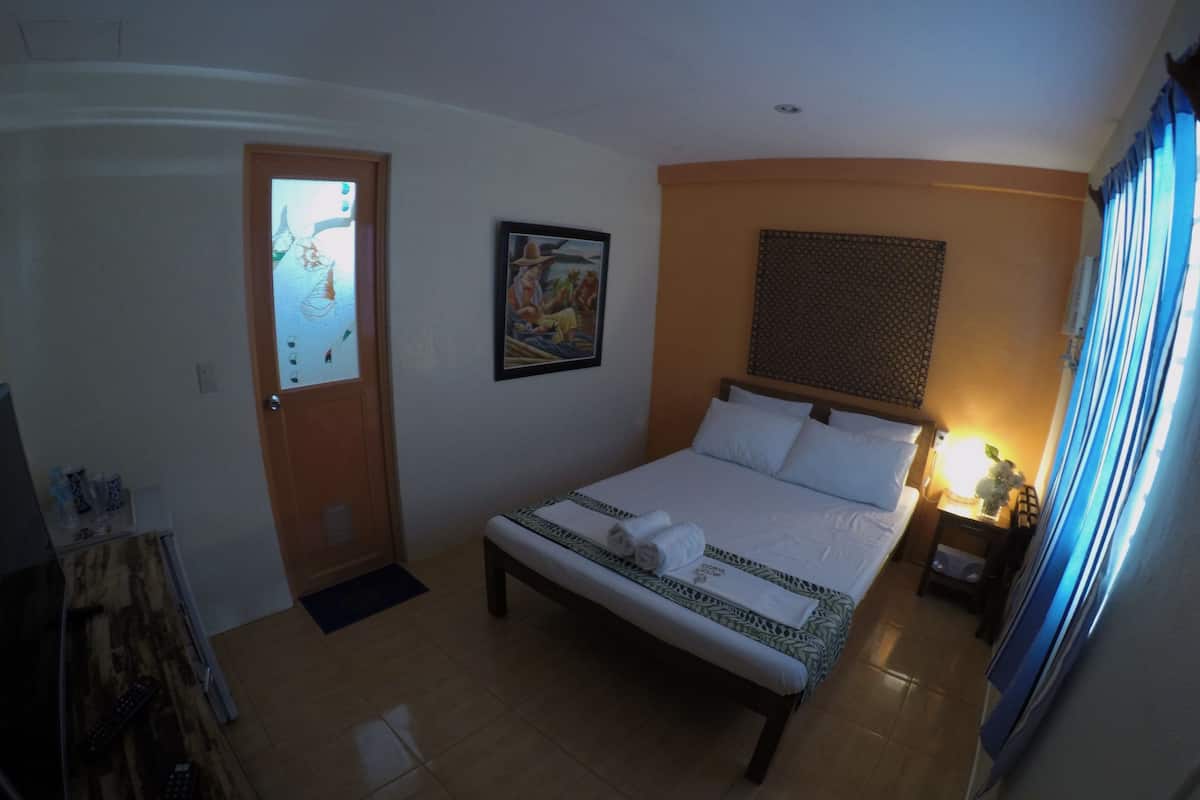 Une chambre d’hôtel avec un lit, un tableau, une porte et une table de chevet avec une lampe.