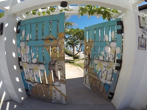Une porte turquoise ornée de motifs floraux et de visages, qui donne sur un sentier.