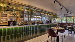 A bar area with shelves of bottles, glasses, and hanging plants. There are tables and chairs for seating. - Premier Inn London Hampstead (London)