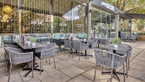 An outdoor seating area with wicker chairs and tables, a covered section with a sign reading 'The Social,' and a view of the street and buildings in the background. - Premier Inn London Hampstead (London)