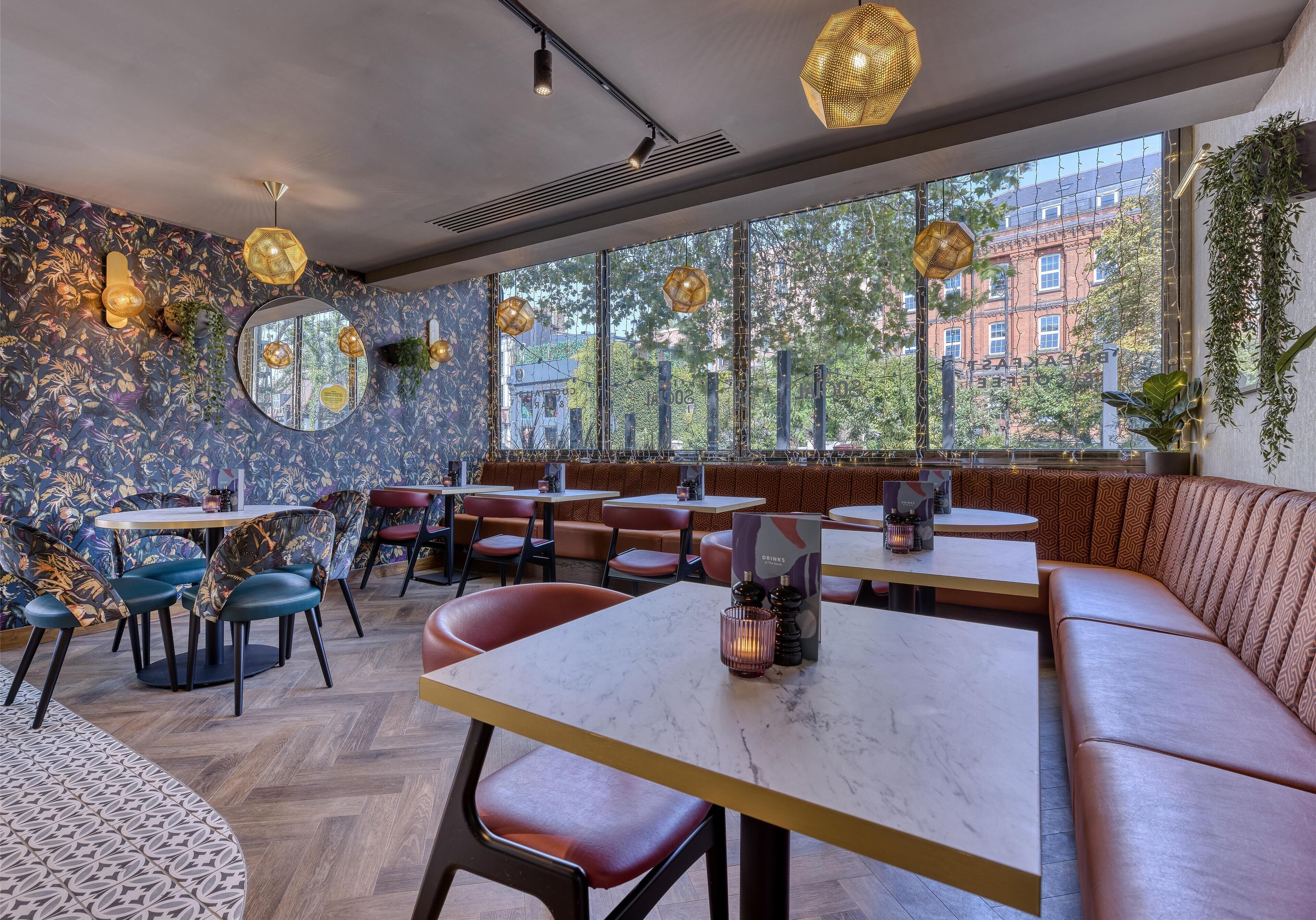 Un interior de restaurante con mesas redondas, asientos acolchados, ventanas amplias e iluminación decorativa.