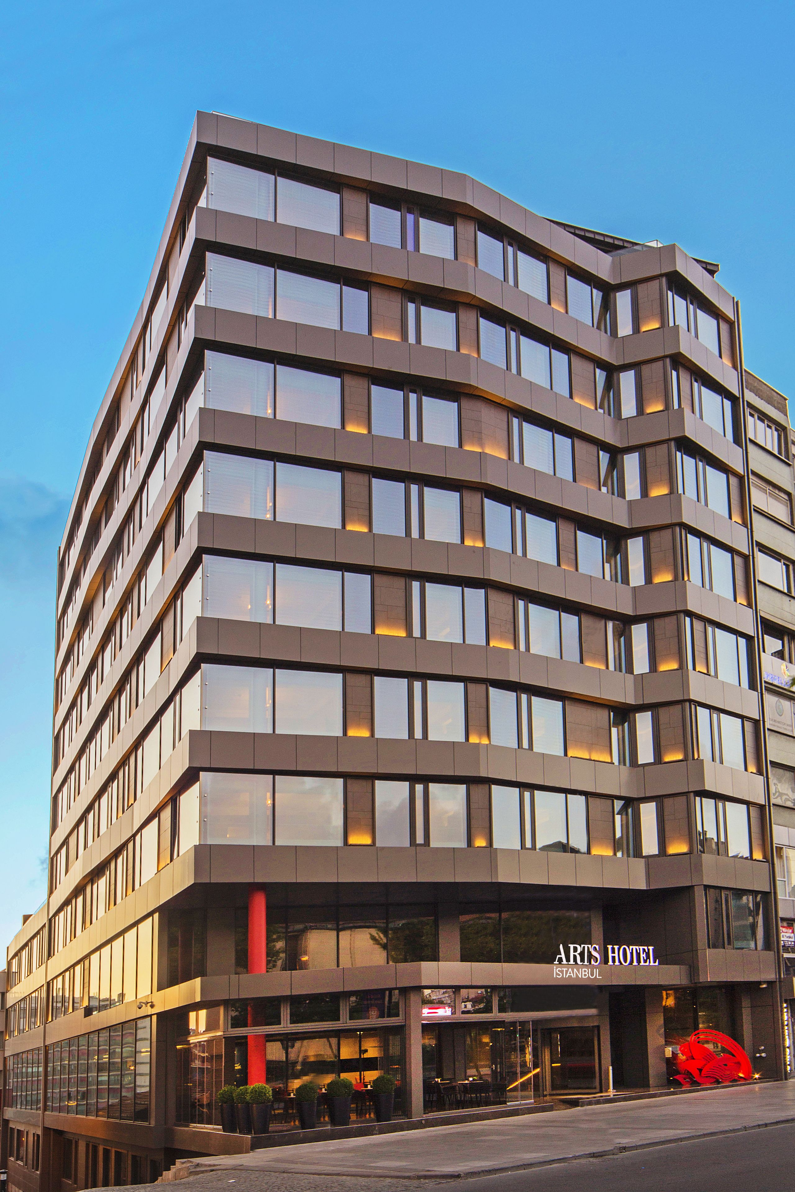 Een modern hotel met een gebogen gevel, meerdere verdiepingen en een opvallende ingang met een rode sculptuur.