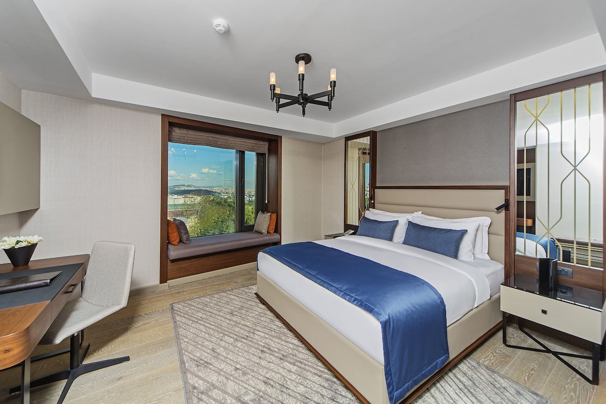 A modern hotel room with a large bed, a desk, and a view of the city.