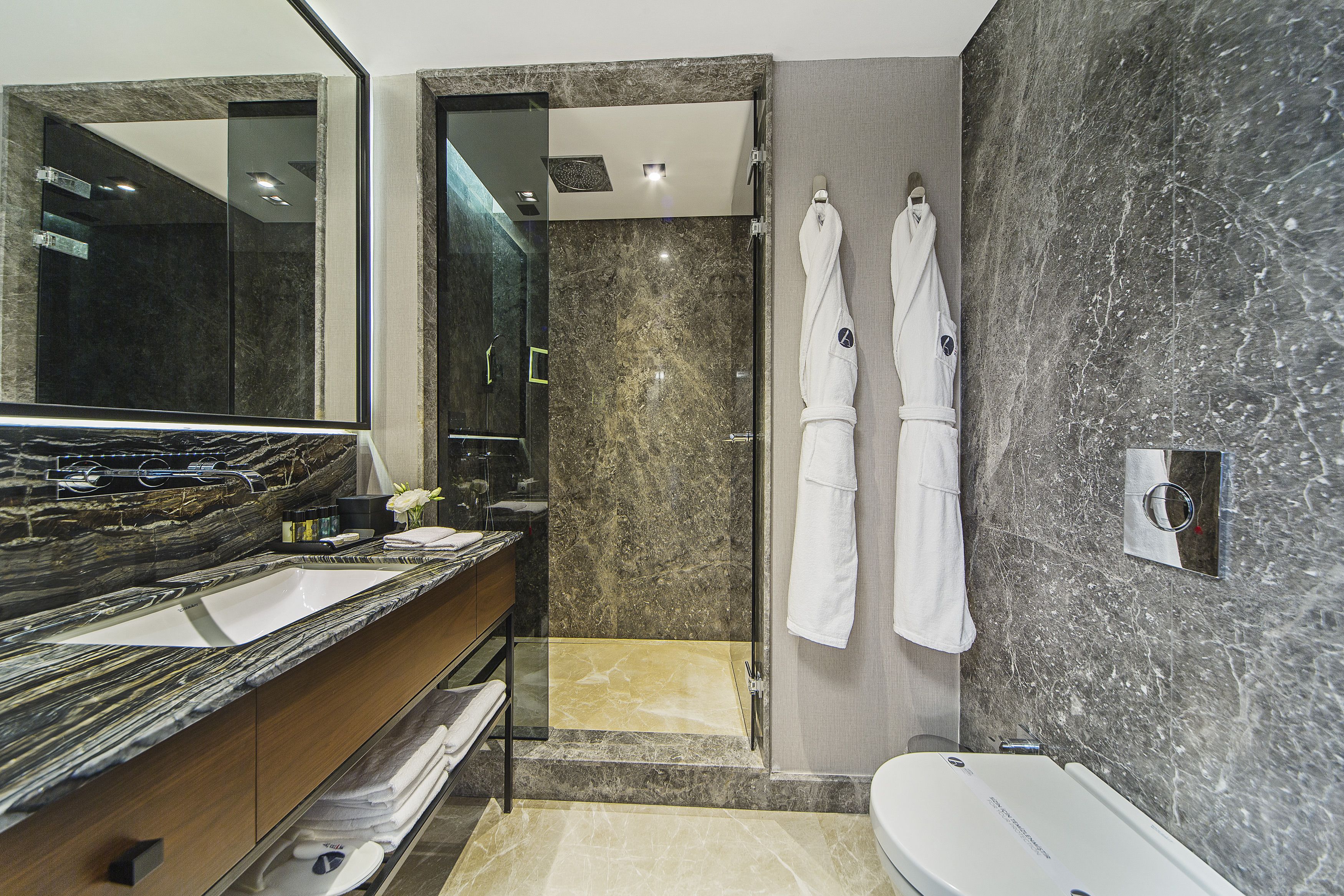 A modern bathroom with a large mirror, two sinks, a shower, and two white towels hanging on the wall.