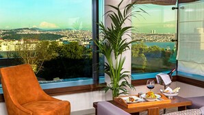 A modern room with a large window, a sofa, a wooden table with a tray of food, and a chair. - Arts Hotel Istanbul - Special Class (Istanbul)
