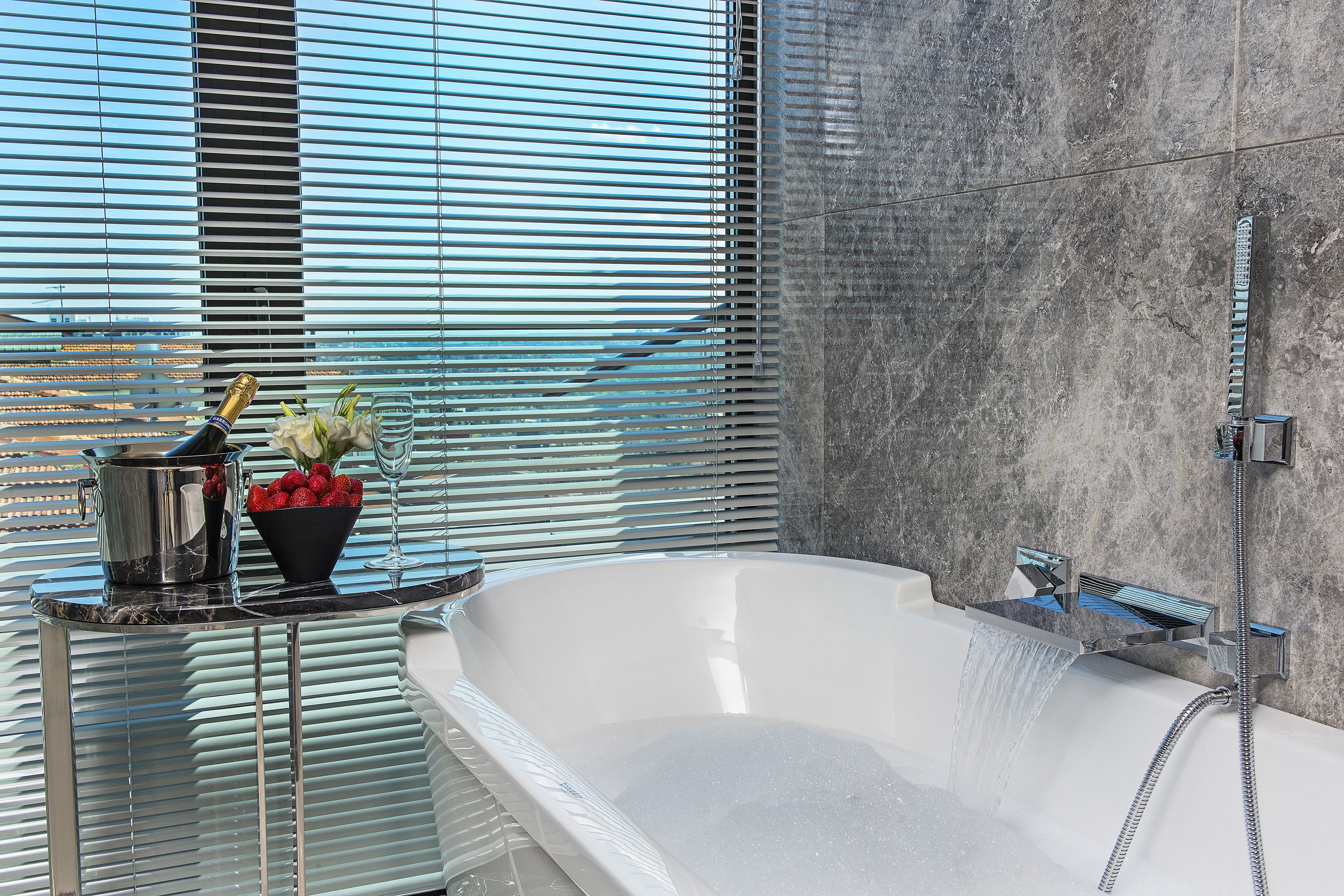 A modern bathroom with a freestanding bathtub, a shower, and a window with blinds.