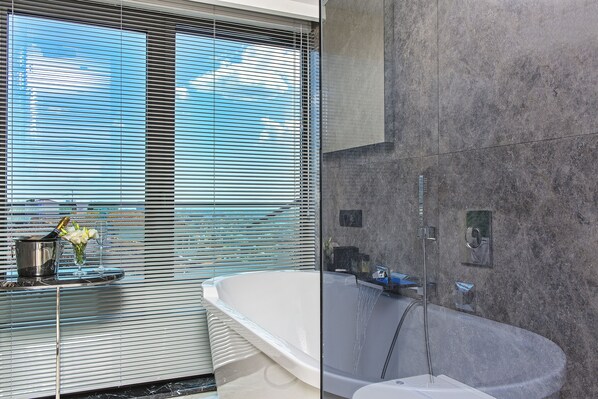 A modern bathroom with a freestanding bathtub, a glass shower enclosure, and a window with blinds.