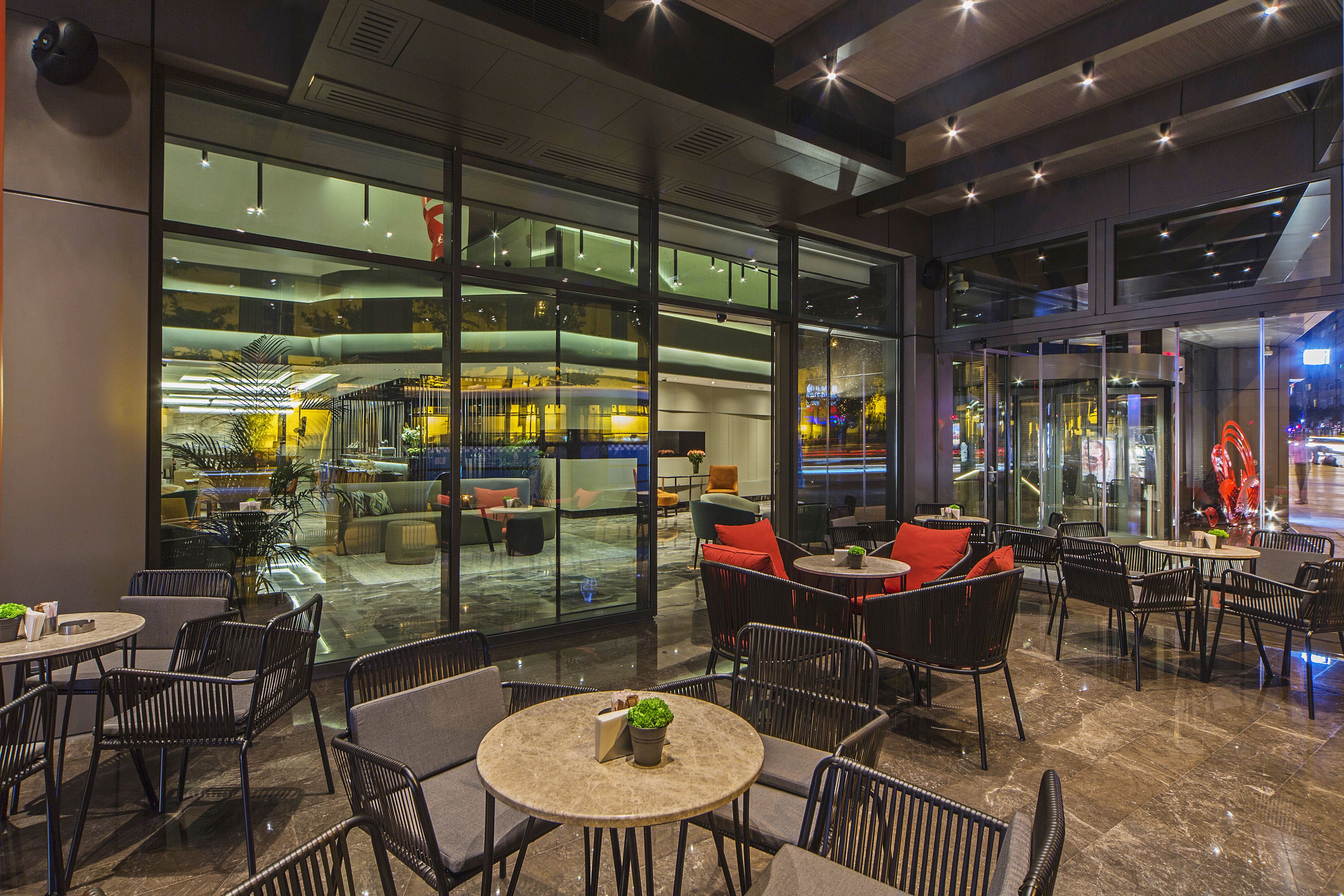 A modern indoor space with glass walls, multiple seating areas, and a visible restaurant or café area.