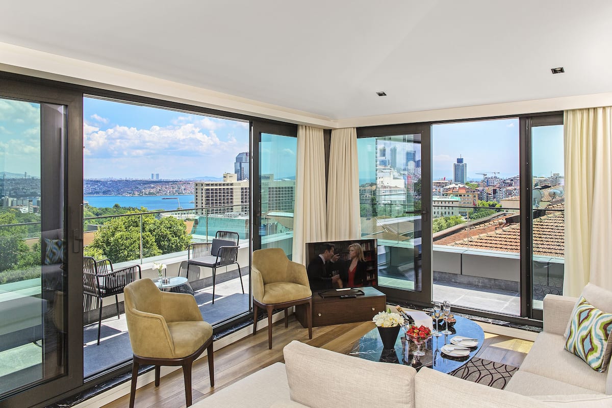 A modern living room with large windows, a sofa, a coffee table, and a TV.
