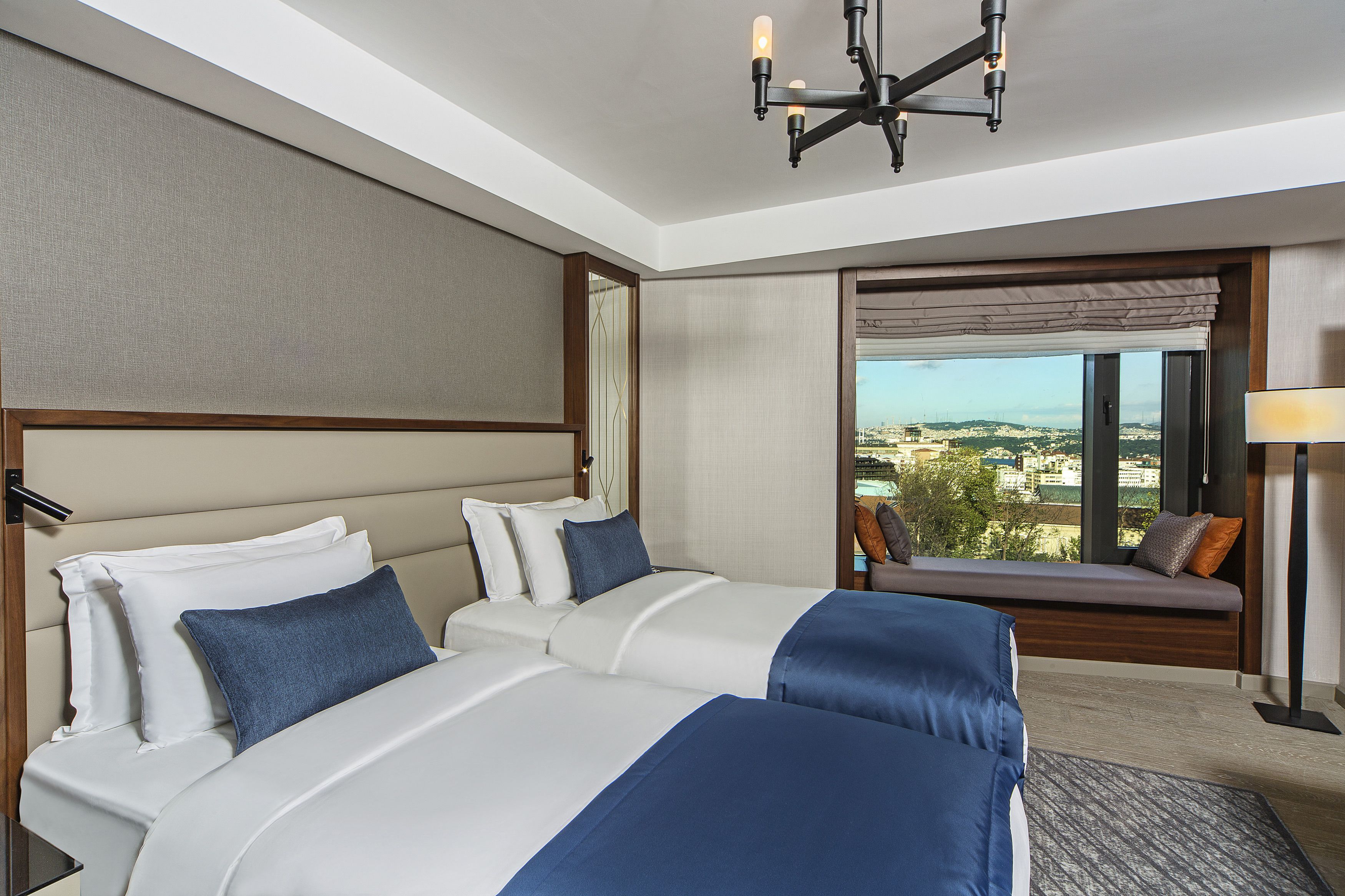 Camera d'albergo con due letti, un'ampia finestra vista, un lampadario e un'area salotto con vista.