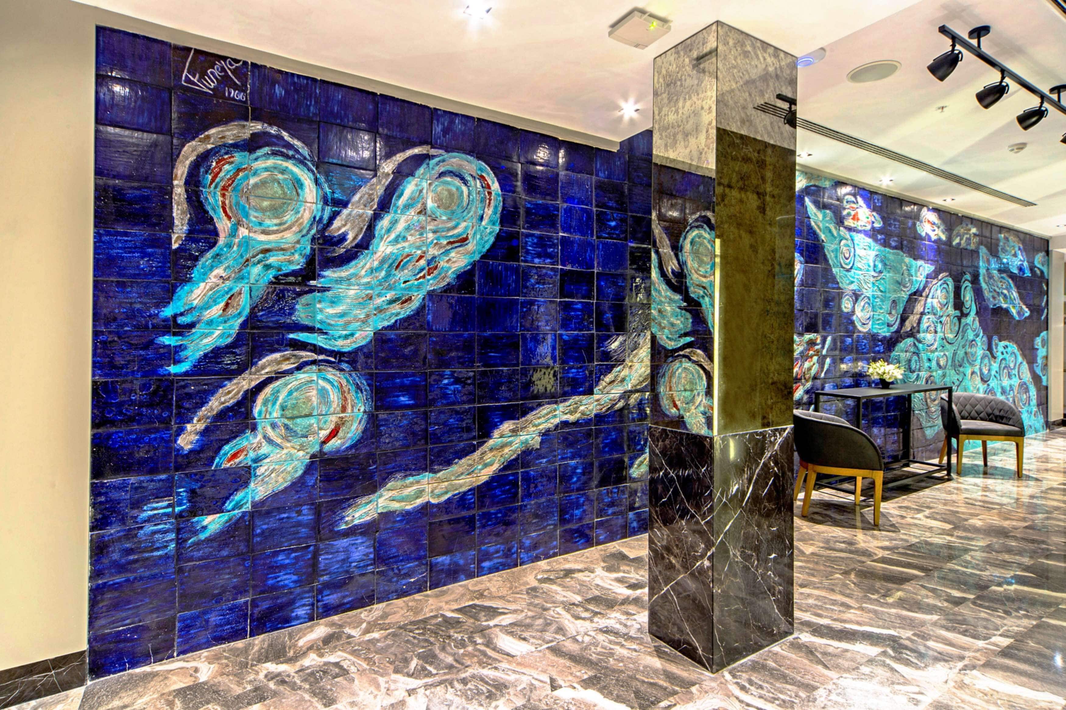 A lobby with a large blue mosaic wall, a marble floor, and a modern light fixture.