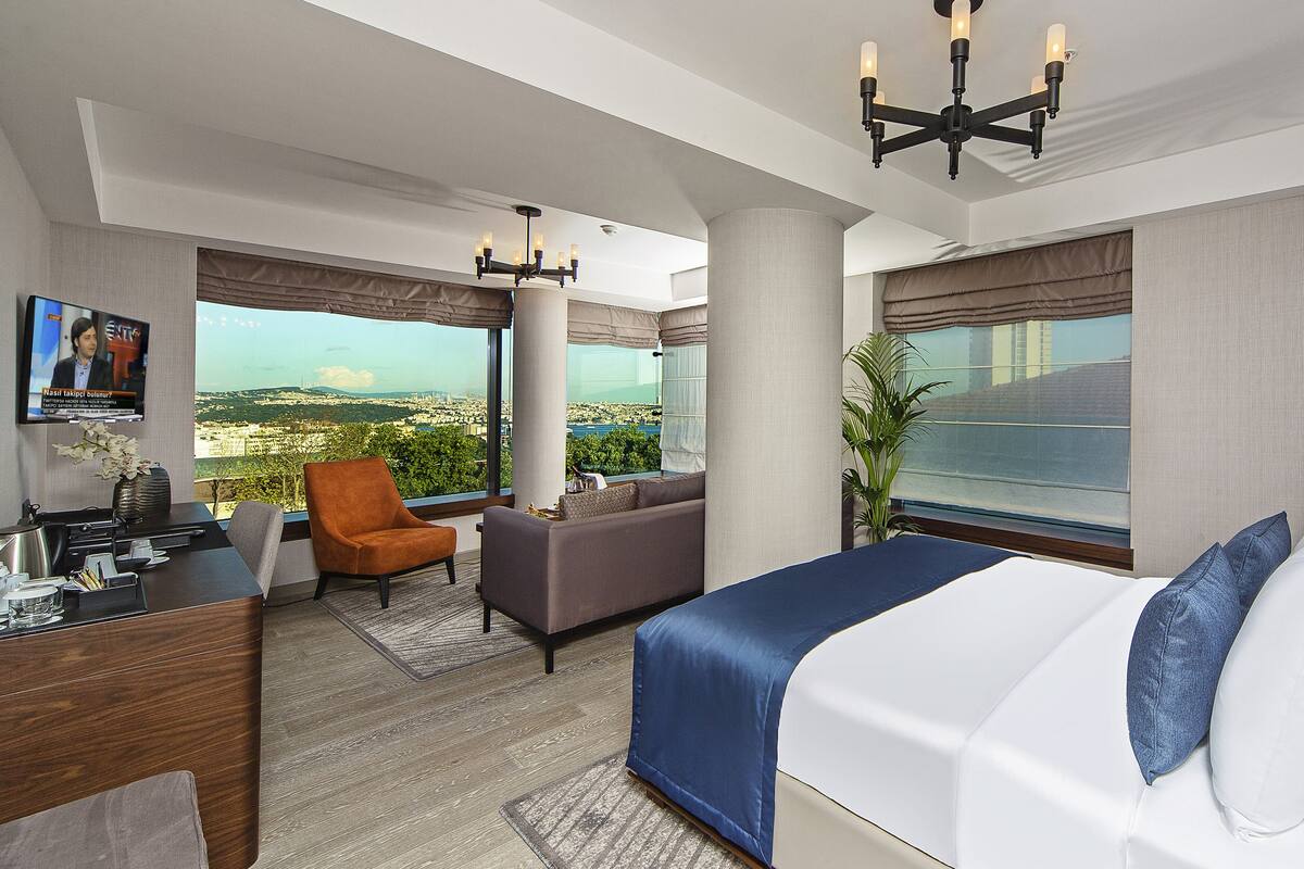 A modern hotel room with a large bed, a sofa, a desk, and a TV.