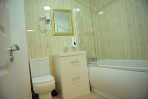 A bathroom with a toilet, a sink with a mirror, and a bathtub. - Canary Heights Apartments (London)