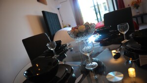 A dining table set with a glass bowl of flowers, wine glasses, and plates, with a chair and a lamp in the background. - Canary Heights Apartments (London)