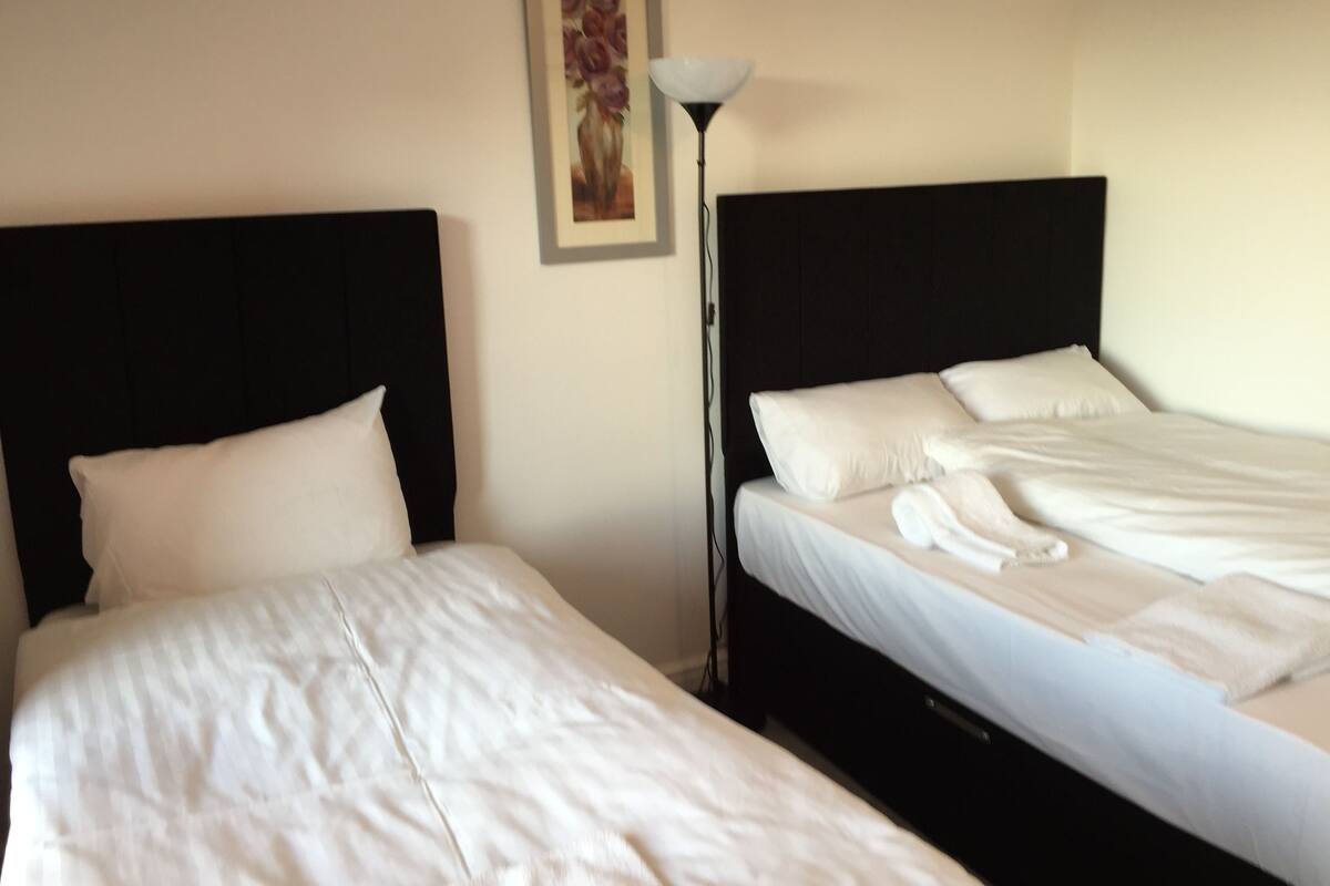 Two beds with white linens, a black headboard, and a painting on the wall.