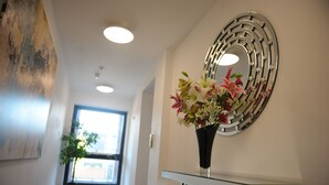 A hallway with a potted plant, a decorative mirror, and a vase with flowers. - Canary Heights Apartments (London)