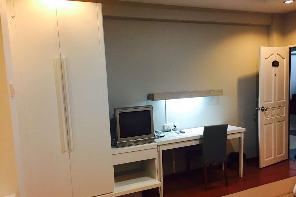 A hotel room with a white wardrobe, a desk with a computer, a chair, and a bed.