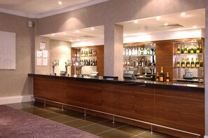 A hotel reception area with a wooden counter, multiple shelves of bottled beverages, a cash register, and a tiled floor. - Premier Inn Bournemouth Central (Bournemouth)