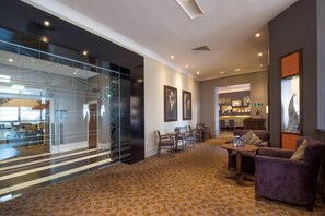 A modern hotel lobby with a glass partition, a patterned carpet, a seating area with sofas and a table, and framed artwork on the walls. - Premier Inn Bournemouth Central (Bournemouth)