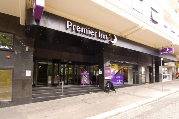 The exterior of a Premier Inn hotel with a prominent sign, a staircase leading to the entrance, and a banner advertising the hotel's opening.
