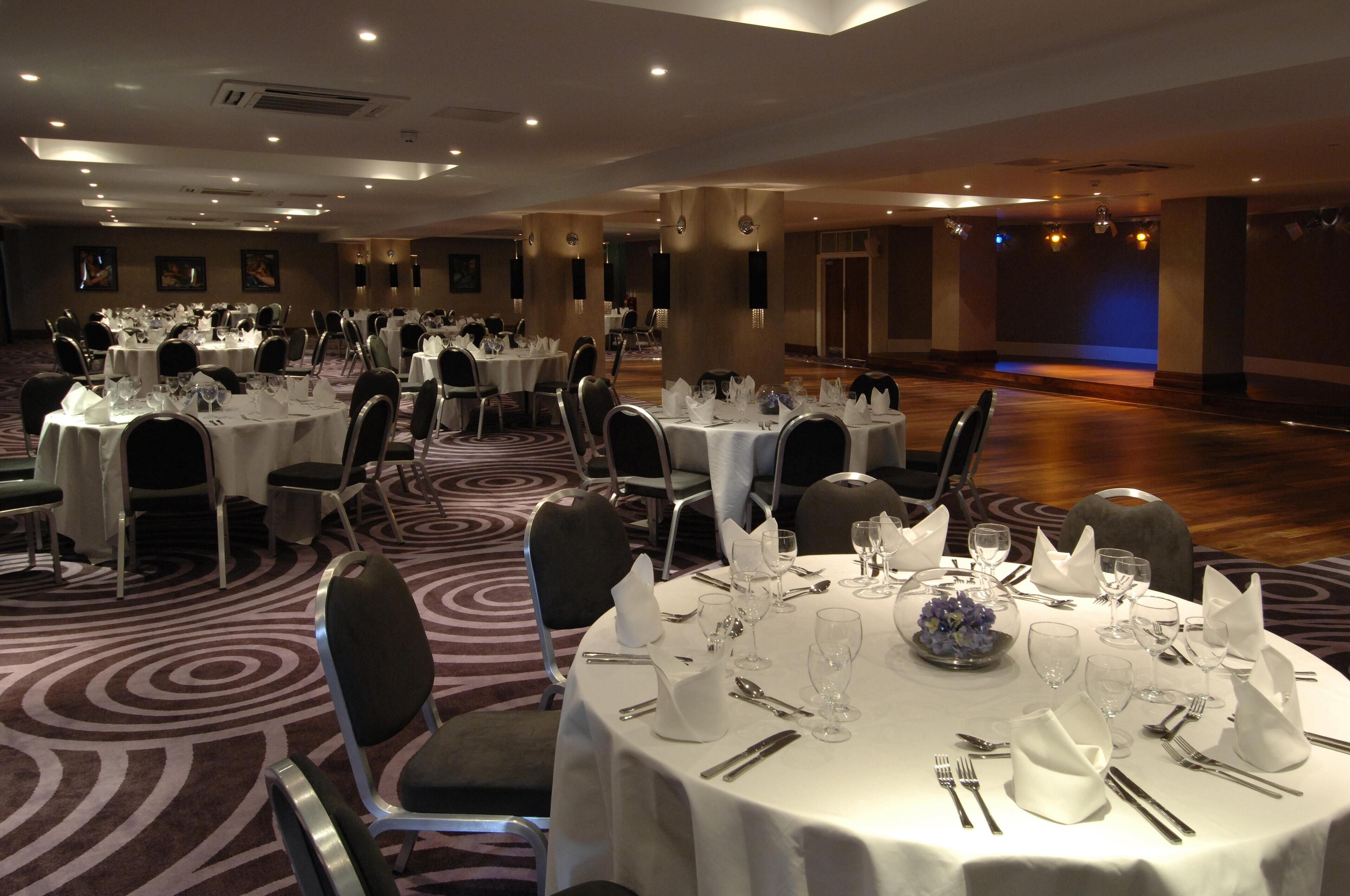 A banquet hall with round tables set for dining, chairs, and a carpeted floor.