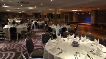 A banquet hall with round tables set for dining, chairs, and a carpeted floor.