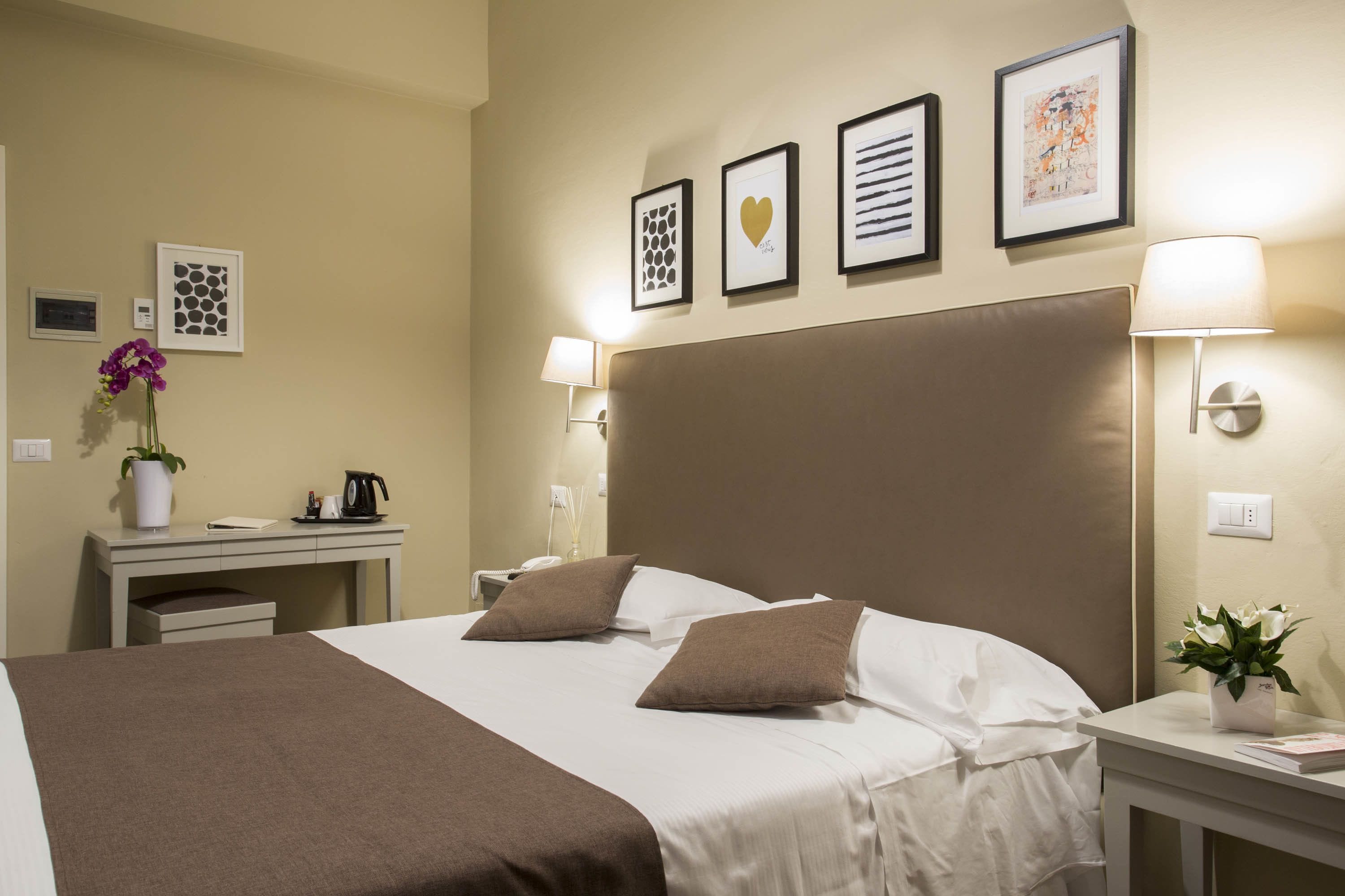 A hotel room with a large bed, a desk with a computer, a coffee maker, and a potted plant.
