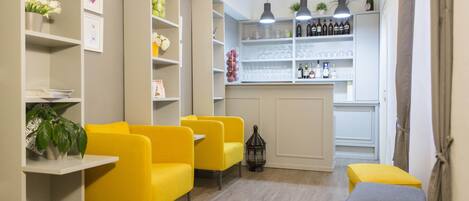 Un interior moderno con sillas amarillas, una mesa pequeña y una zona de bar con estantes llenos de botellas y vasos.