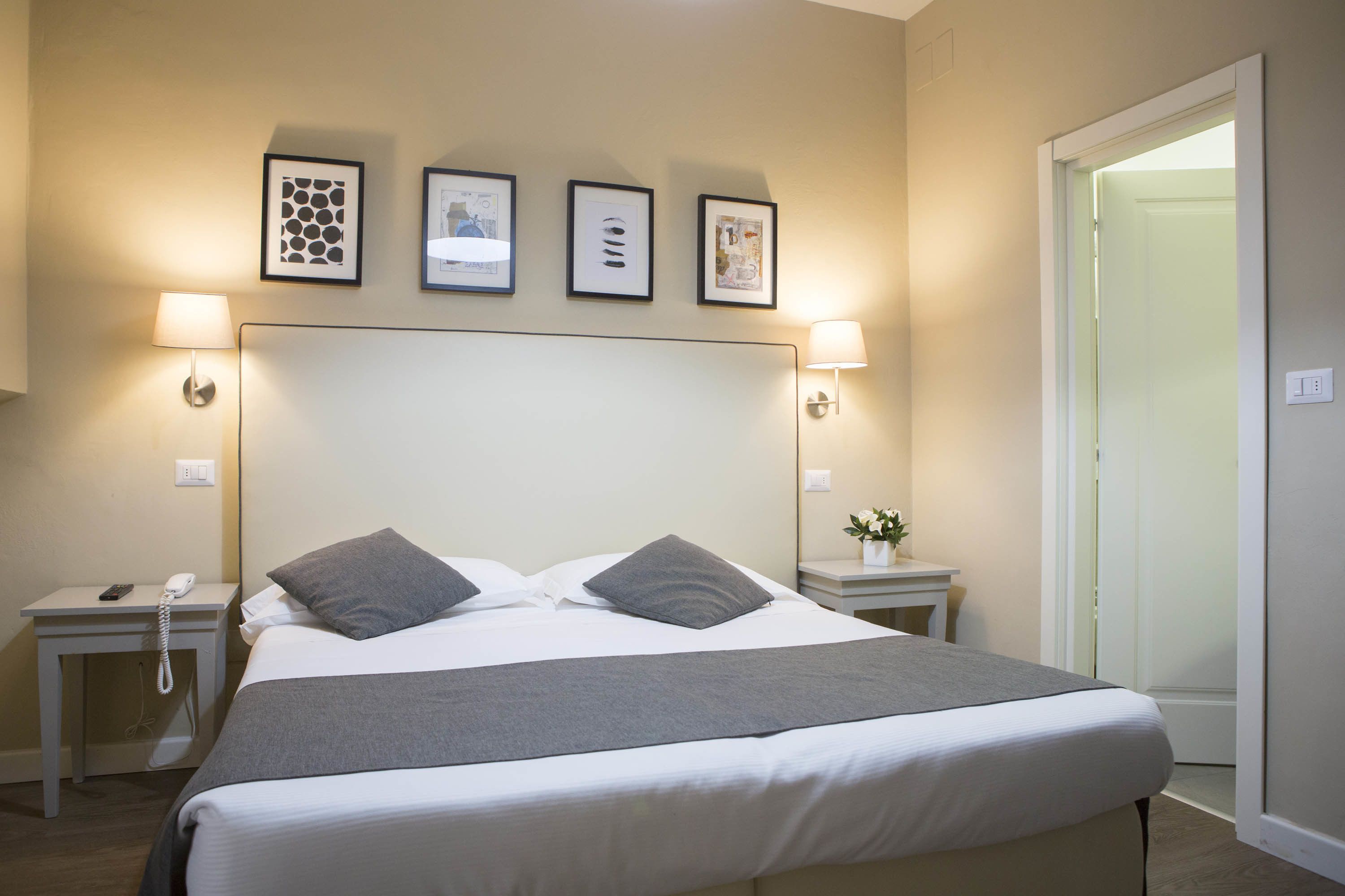 A neatly made bed with a grey blanket and pillows, a bedside table with a lamp, and framed pictures on the wall.