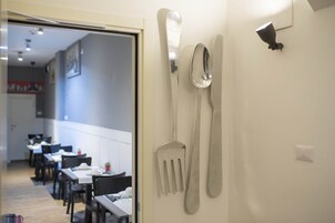 Zona pranzo con tavoli e sedie, un set di coltelli montato a parete e un interruttore della luce.