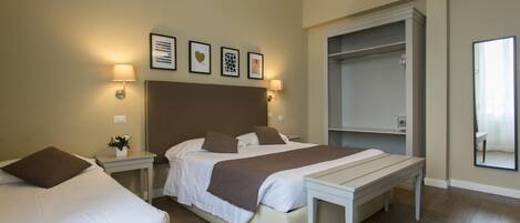 Habitación de hotel con una cama grande, mesitas de noche, un banco, armario y obras de arte colgadas en la pared.
