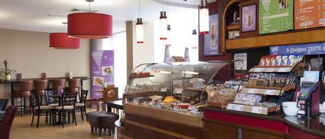 Un café avec un sol à carreaux, un comptoir où sont exposées des pâtisseries et un tableau affichant le menu.
