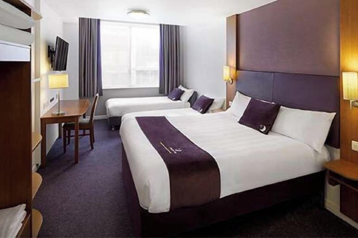 Quarto de hotel com duas camas, uma escrivaninha, uma cadeira e uma televisão.