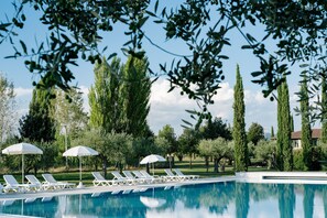 A pool area with lounge chairs and umbrellas, surrounded by trees and a clear sky. - Valle di Assisi Country Apartments (Assisi)