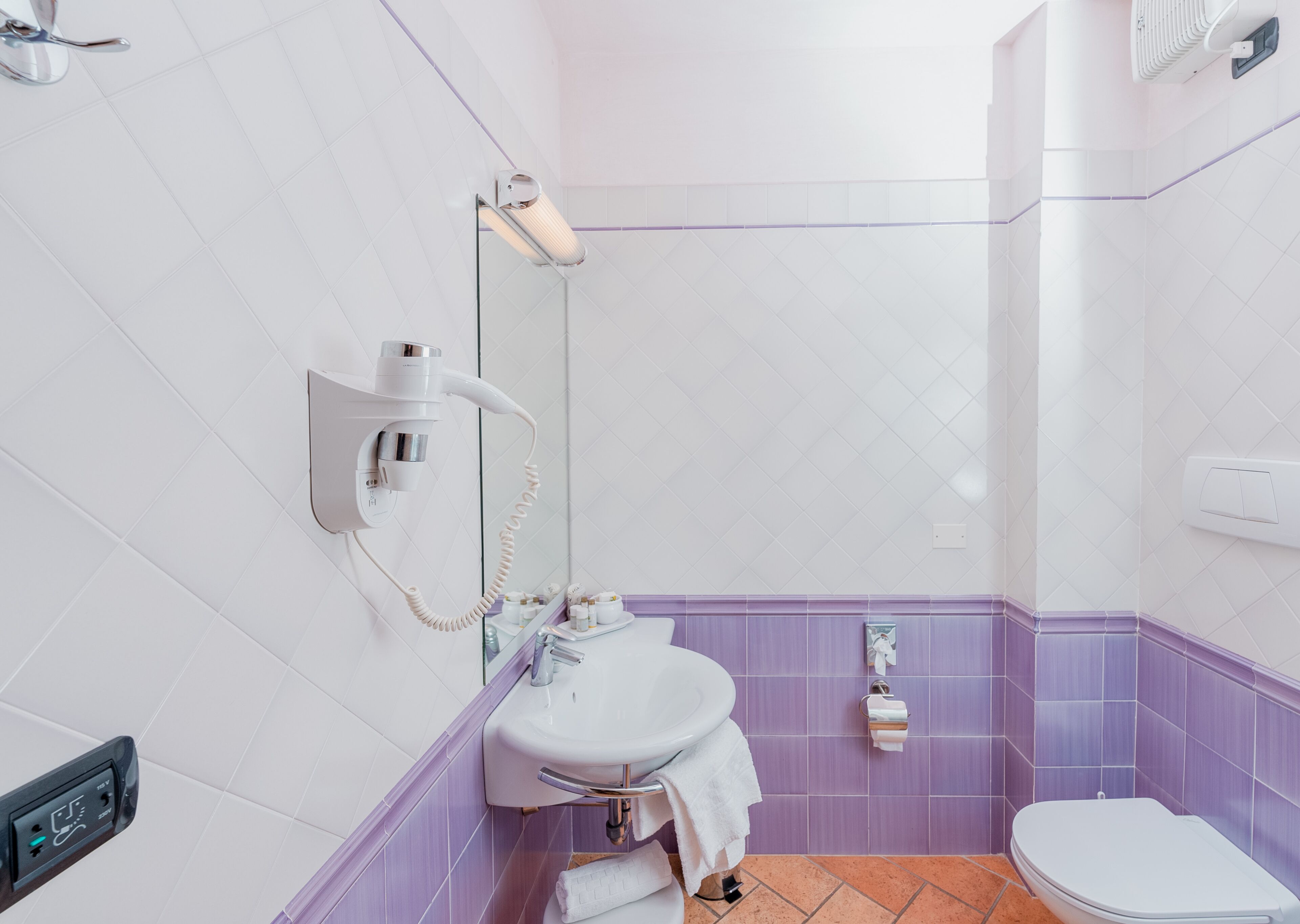 A bathroom with a white sink, a mirror, a hairdryer mounted on the wall, and a toilet.