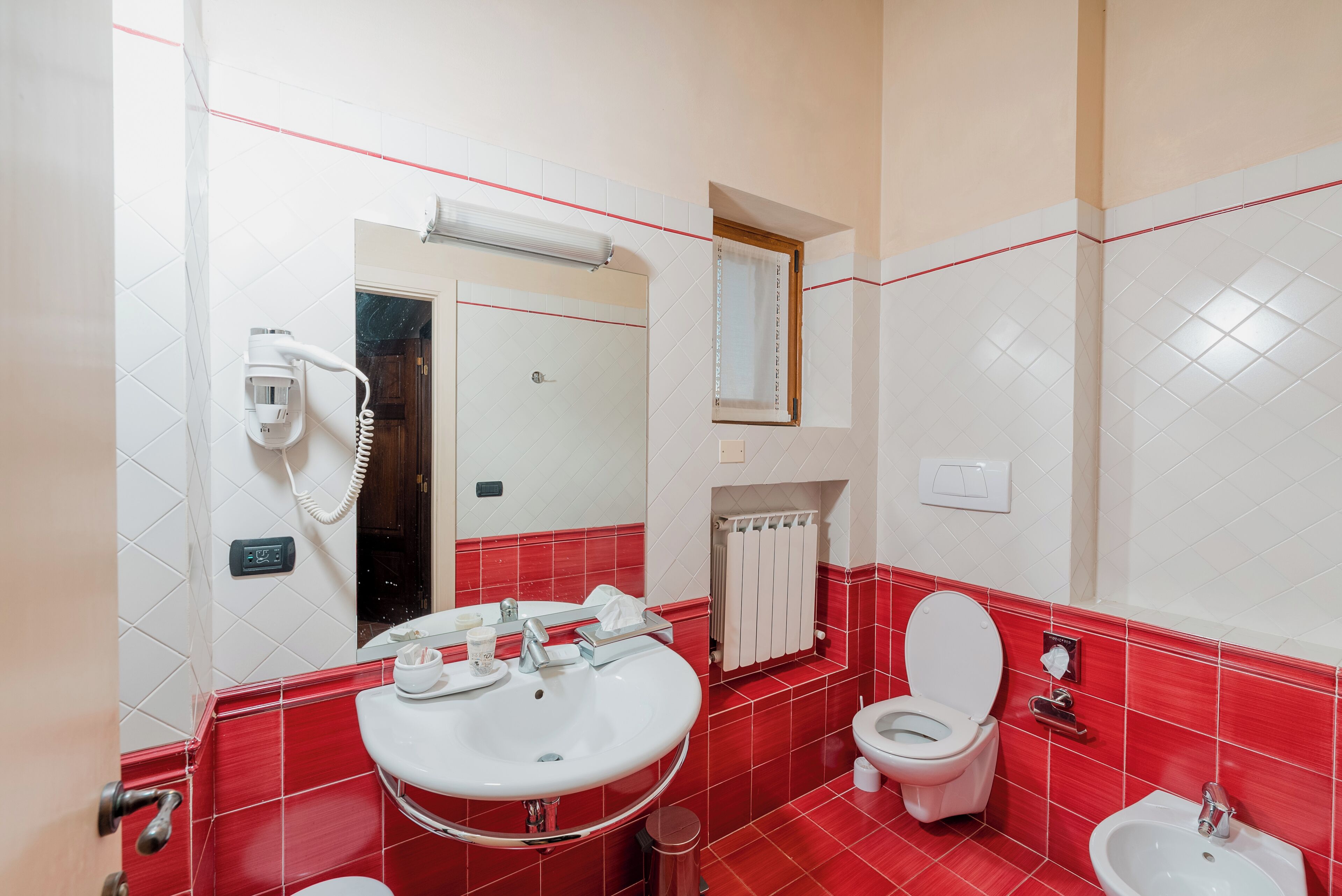 Une salle de bain avec un sol carrelé en rouge et blanc, un lavabo blanc, des toilettes et un bidet.