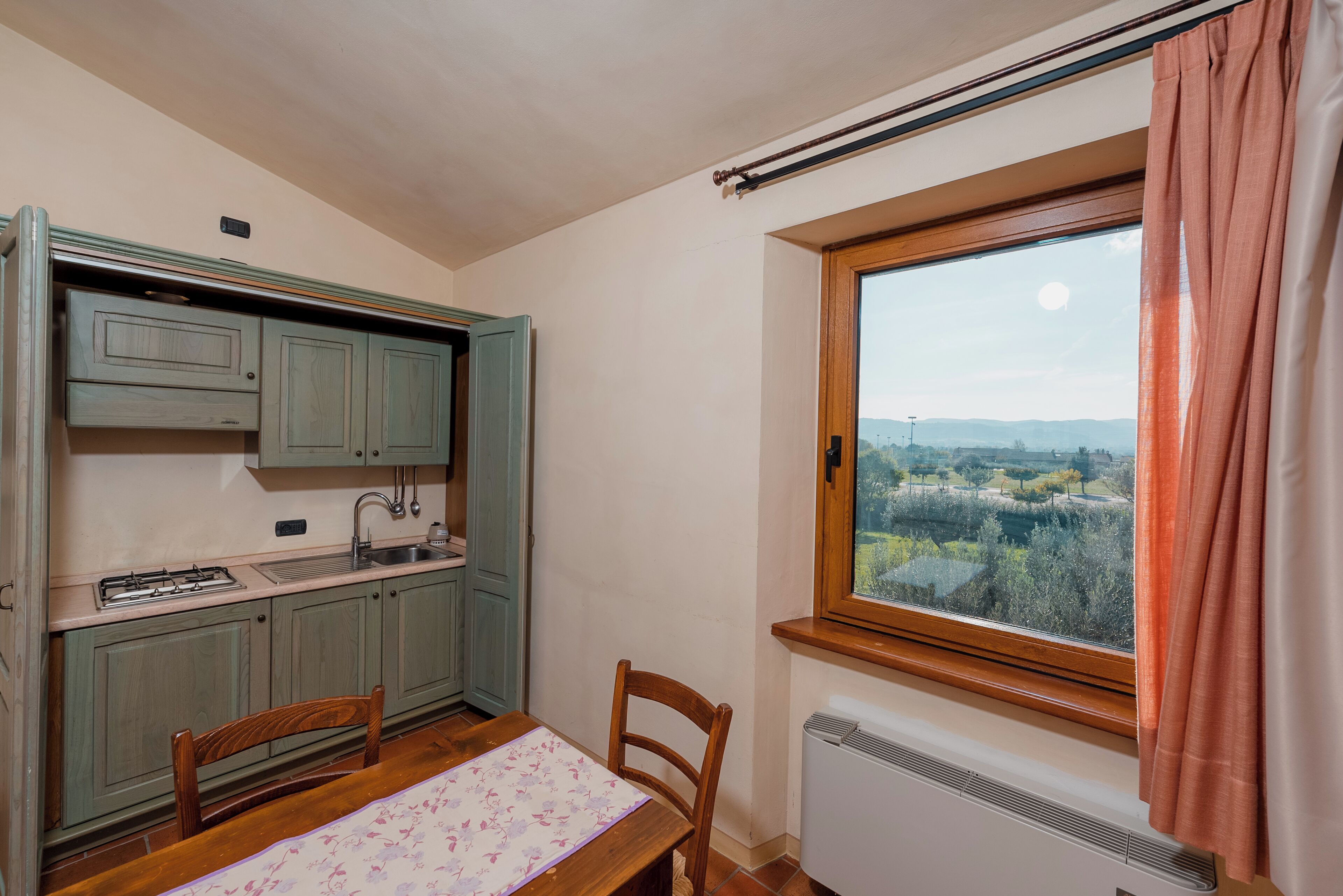 Une petite cuisine avec une table et des chaises, une fenêtre donnant sur la campagne et un radiateur.