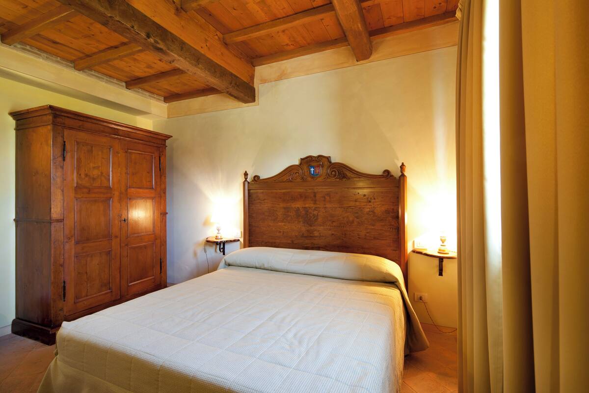 A bedroom with a wooden headboard, a large wardrobe, and bedside lamps.