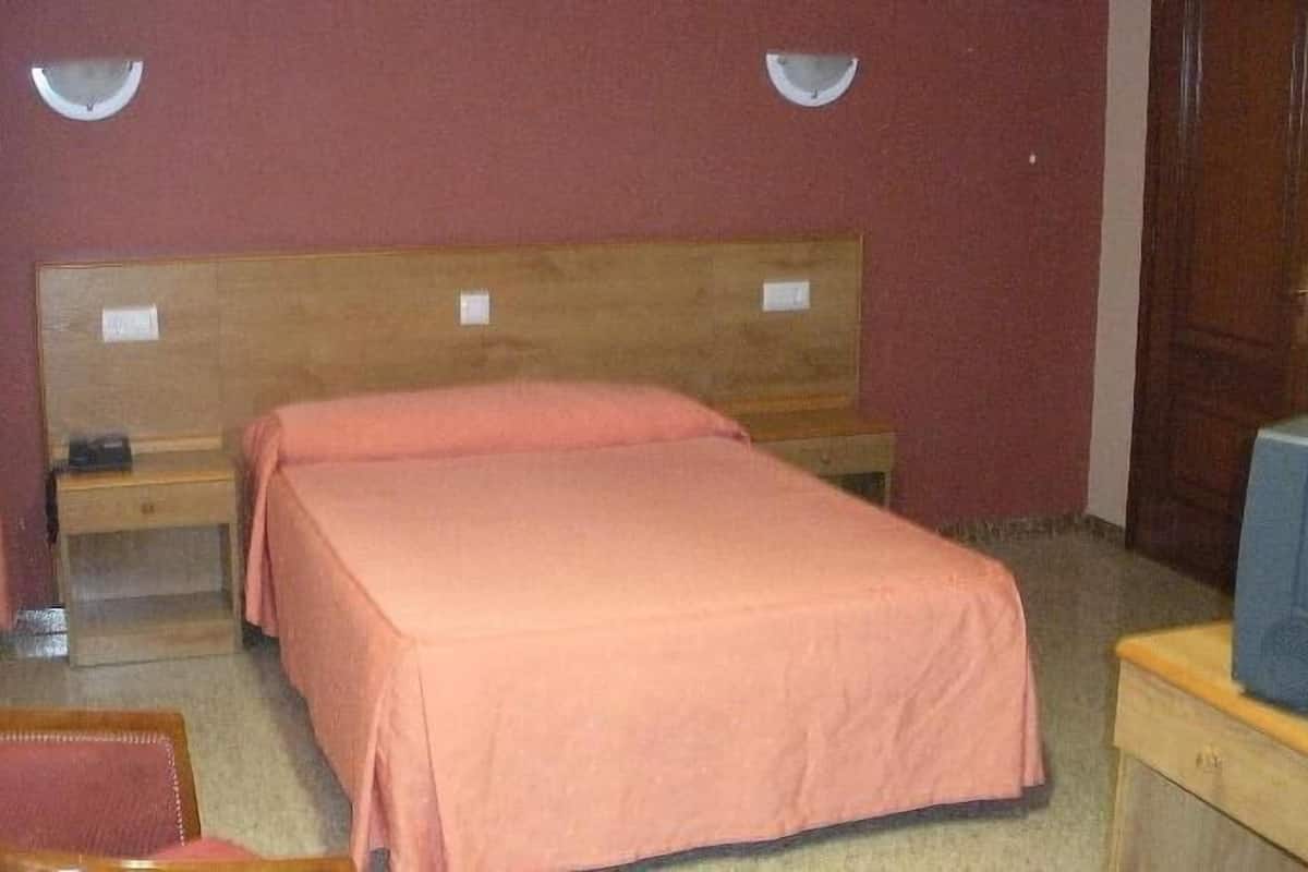 A single bed in a room with a wooden headboard, a nightstand, a chair, and a small table with a blue object on it.