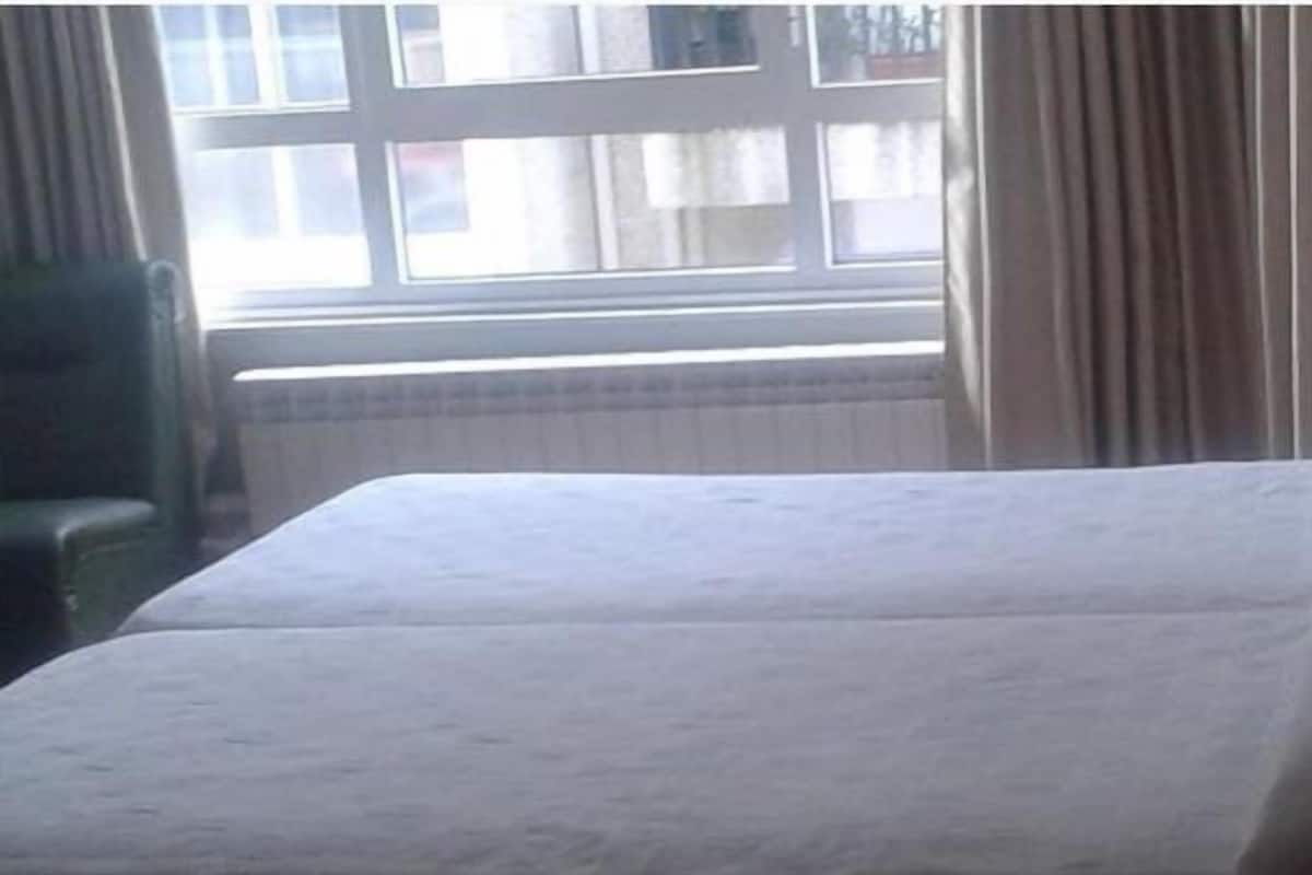 A hotel room with a bed, a chair, and a window with curtains.