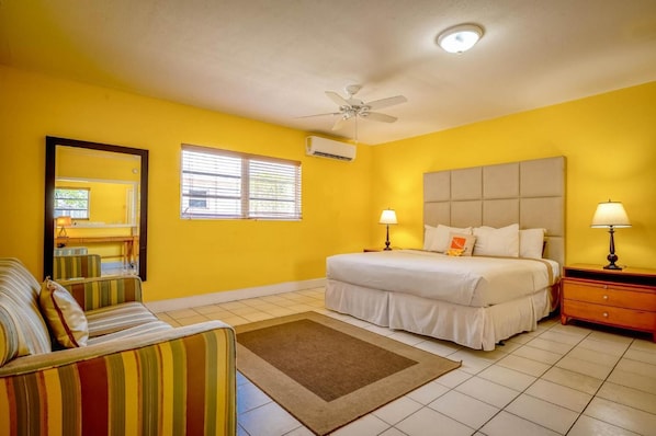 Un dormitorio con cama, mesitas de noche, ventilador de techo y ventana con persianas.